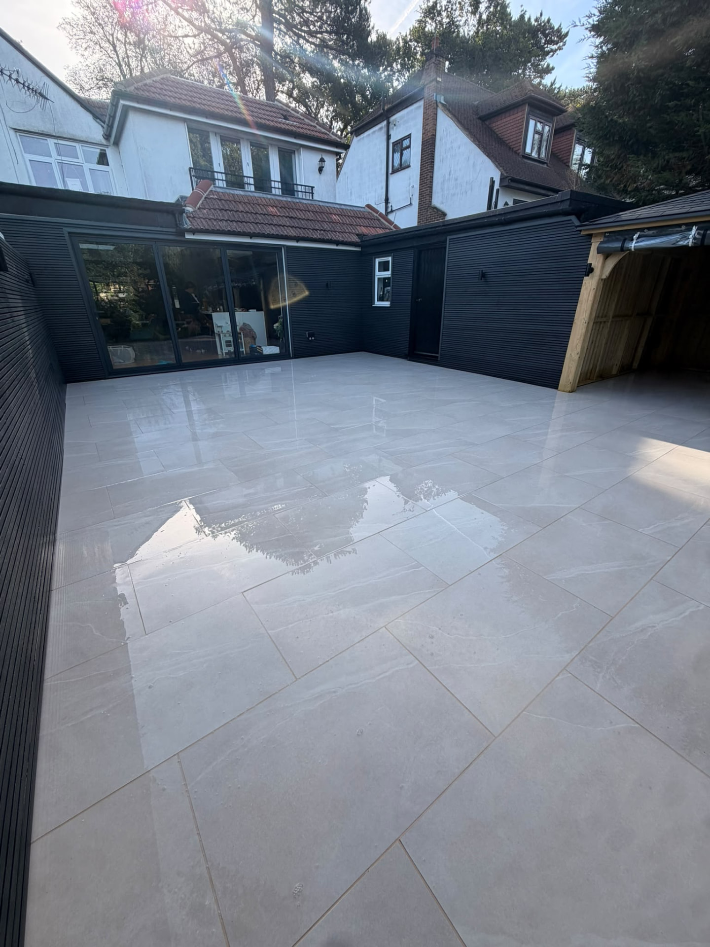 Large porcelain patio in front of black composite cladding and sliding doors